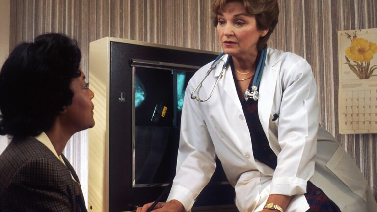 doctor sitting on desk talking to sitting woman