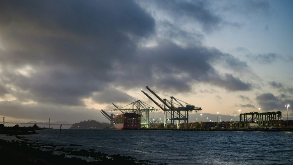 Industrial cranes at a port by the water at dusk.