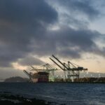 Industrial cranes at a port by the water at dusk.