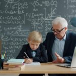 Elderly man teaching young boy math at desk.