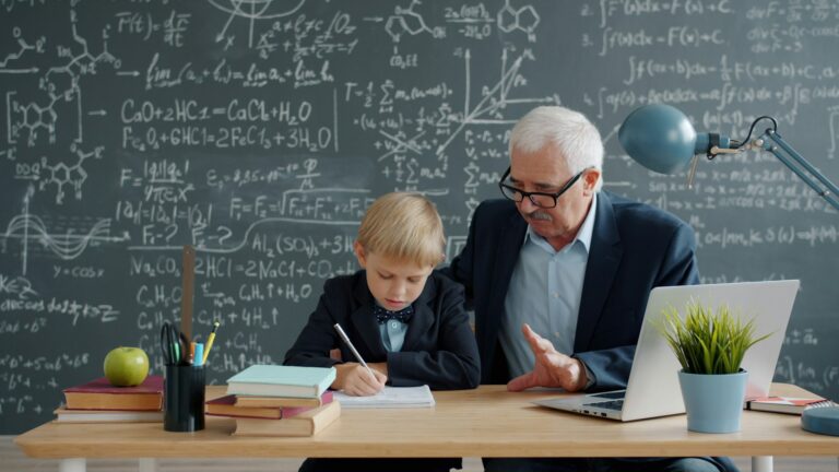 Elderly man teaching young boy math at desk.