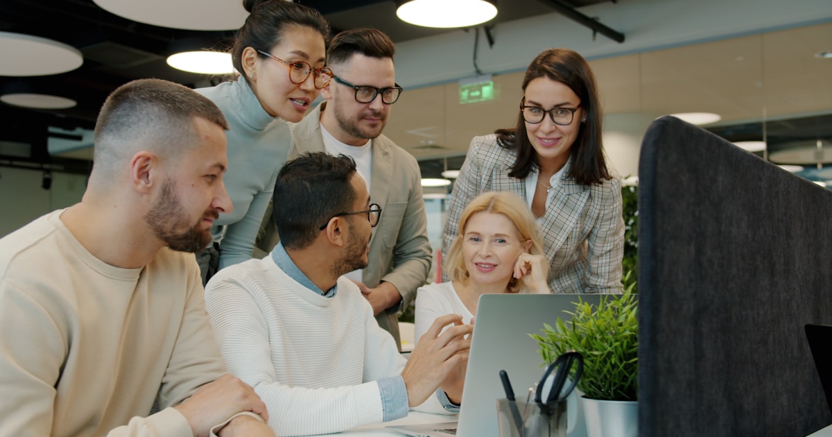 Diverse team collaborating around a laptop in office.